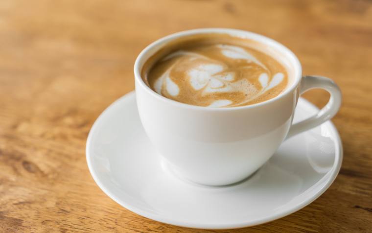 Café con leche en taza blanca sobre mesa de madera
